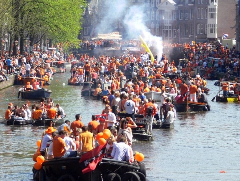 Groups of people dressed in orange on various boats during King's Day on the Amsterdam canals