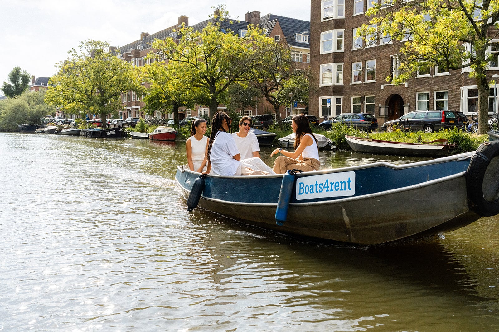 Three women and a man sailing on a sloop through the Amsterdam canals.